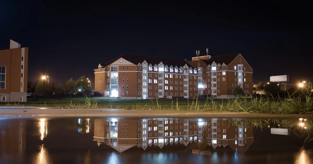 Edificios del campus de la Universidad Emanuel de Oradea (Rumanía), de noche y reflejados en el agua (foto de 2022)